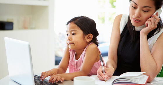 Mother working from home while daughter types on laptop next to mother