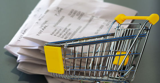 A shopping cart superimposed in front of a stack of paper receipts.