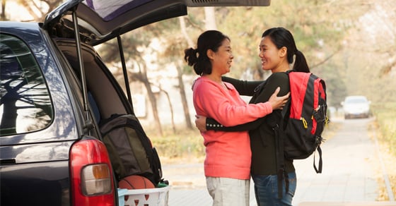 A daughter wearing a backpack hugging her mother in front of a car with the trunk open