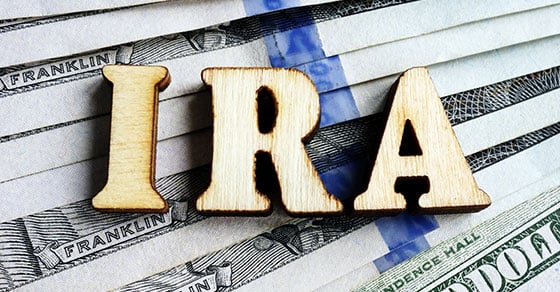 Wooden cutouts of letters that spell "IRA" resting atop some United States paper currency