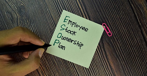 A hand holding a felt tip pen writing on a sticky note that says "Employee Stock Ownership Plan"