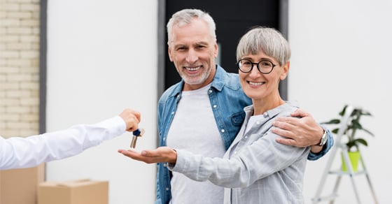 Two people smiling while being handed a set of keys by a person out of frame