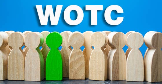 A group of simple, uniformly-colored wooden figurines with a single one colored green in the front row under the letters "WOTC"