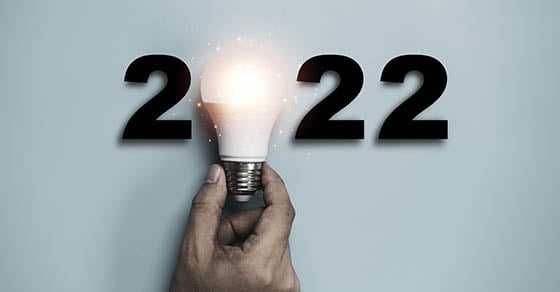 The numbers "2022" but the zero is represented by a shining light bulb held up by a hand