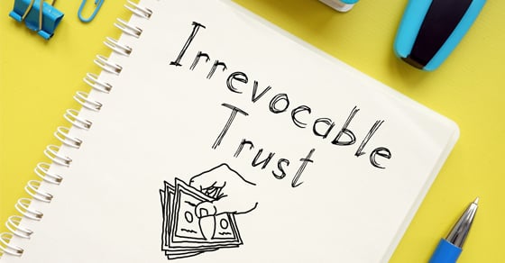 Photo of a desk with writing utensils and paperclips focusing on a sketchbook that has a drawing of a hand holding money beneath the words "Irrevocable Trust"