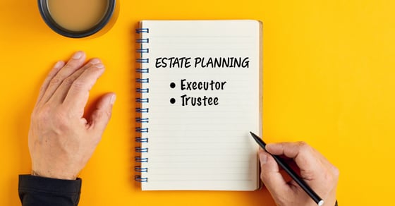 A yellow surface with a coffee mug, notebook, and a man's hands holding a pen. The notebook says 'estate planning' and displays a list with 'executor' and 'trustee'.