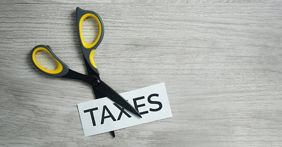 A pair of scissors cutting a piece of paper with the word "Taxes" written on it.