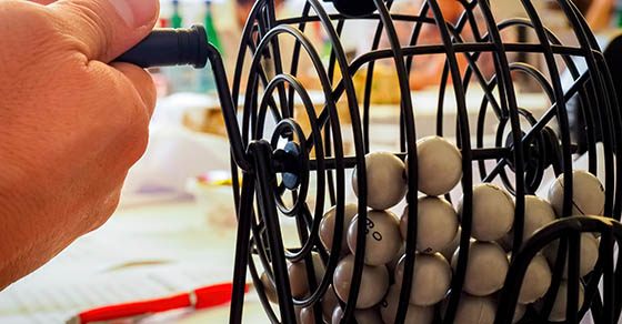 An image of a hand that appears to be turning a bingo cage with the bingo number balls inside it.