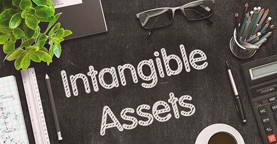 A black desk scattered with various office supplies and white text that reads "Intangible Assets"