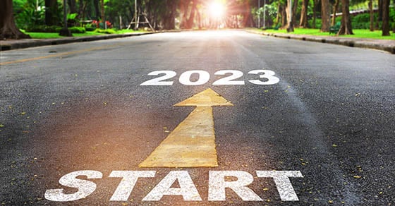 A paved road with a sunset or sunrise on the horizon, "2023 Start" is painted on the road with a yellow arrow pointing toward the sun.