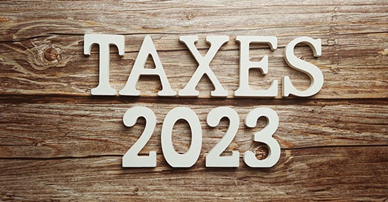 "Taxes 2023" in white text on a wooden background.