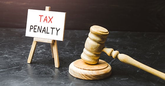A small canvas with the words "Tax Penalty" on it next to a gavel on a black marbled table.
