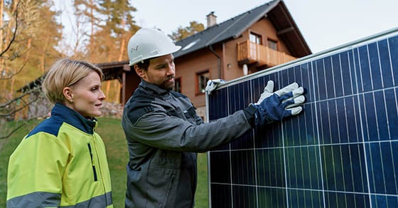 A woman and an electric worker looking at a solar panel while standing outside of a home.