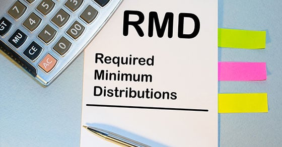 A view of a surface that has a calculator, sticky notes, and a piece of paper on it. The paper reads "RMD - Required Minimum Distributions".