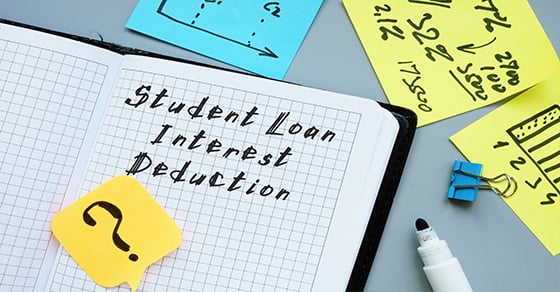 A surface scattered with sticky notes, paperclips, and other items. There is an open notebook with "Student Loan Interest Deduction" written on it.