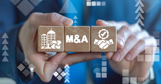 An image of someone holding three wooden blocks together in a row, they all have something printed on them in white text. The middle block reads "M&A".