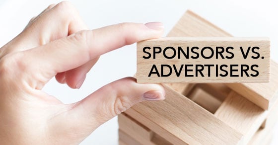 A hand holding a wooden block labeled 'SPONSORS VS. ADVERTISERS'