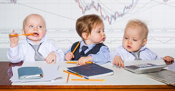 Three babies wearing business attire sitting at a table with office supplies.