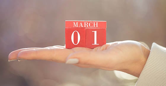 A hand holding red calendar blocks that show the date March 1st.