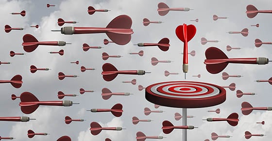 A lot of red darts and one target in a cloudy sky. The target and one dart are perpendicular to the other darts.