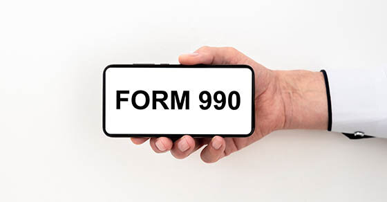 A hand holding a phone that's screen reads "FORM 990".