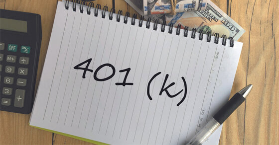 A desk with a calculator, notebook, and pen on it. The notebook reads '401 (k)'