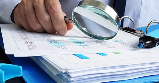 A person looking at paperwork very closely with a magnifying glass.