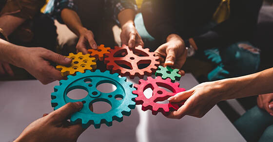 People holding different colored cog wheels together in the middle of a circle.