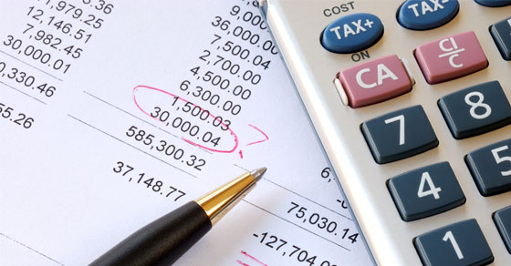 A pen and a calculator on top of a document with various totals on it with "$30,000" circled in red ink.