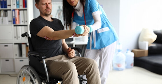 A healthcare worker helping someone in a wheelchair lift weights to workout.