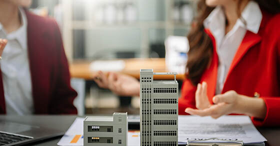 Two mini figures of buildings in focus with two people sitting at a table out of focus behind them.