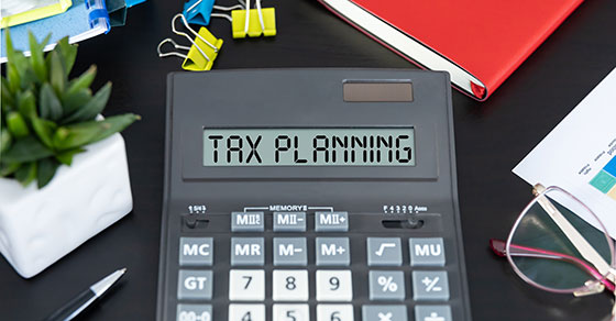 A calculator on a cluttered desk that's screen reads 'TAX PLANNING'.