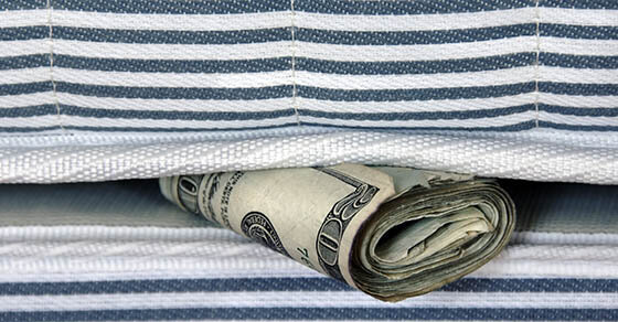 A roll of cash in between what appears to be a mattress and box spring.