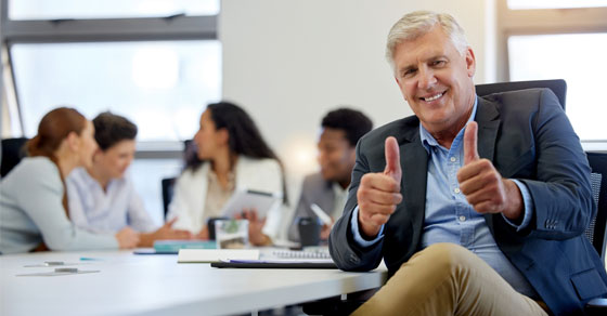 A man giving a thumbs up to the camera while a small group of people talk behind him.