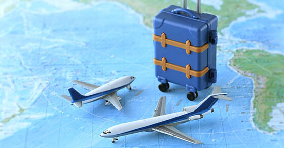 A toy suitcase sitting on a world map with two planes around it.