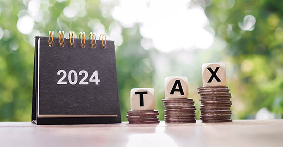 A small 2024 calendar book sitting next to 3 stacks of coins with blocks on them that read 'TAX'.