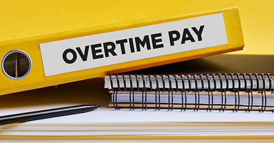 A binder on top of some notebooks that says "Overtime Pay" on the label along its spine.